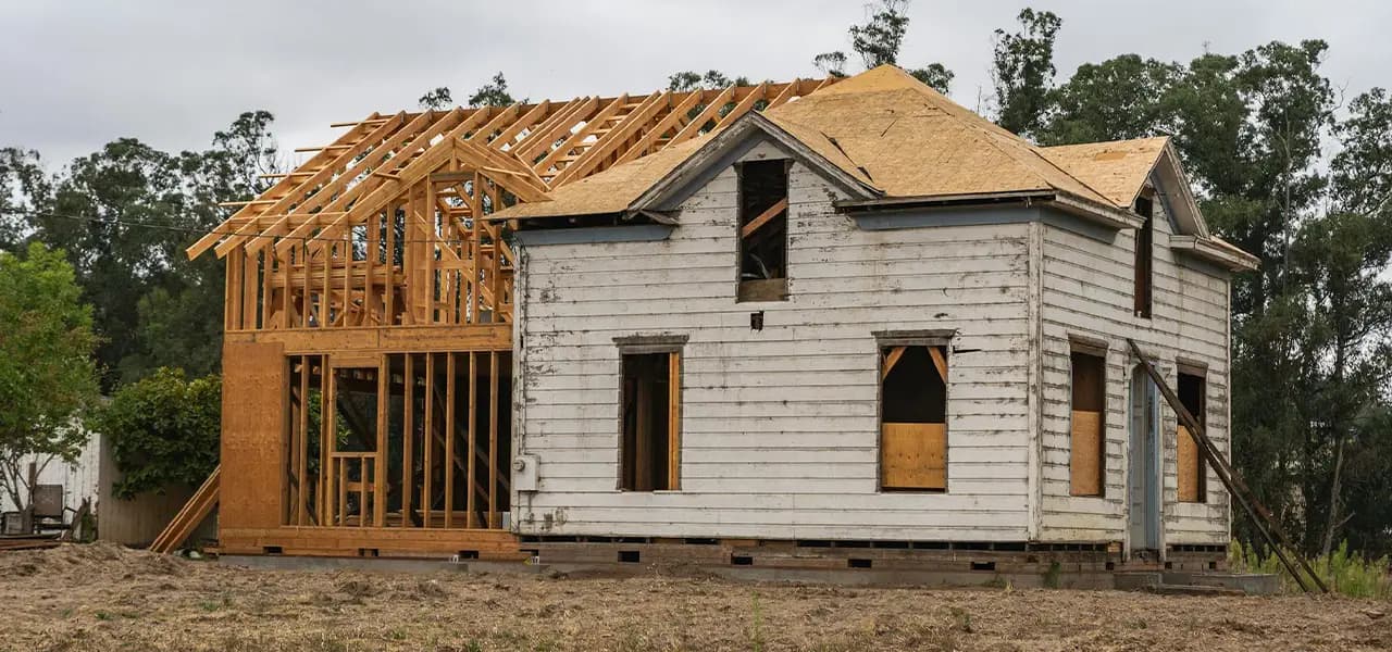 Construction crew rebuilding a fire-damaged house with new framing and roof repairs in progress